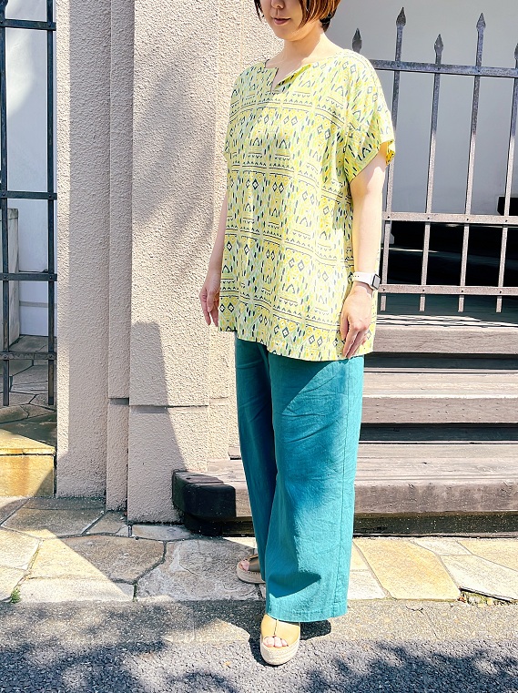 黄色をベースカラーにしたバティックプリントが魅力的なタバサオリジナル素材のブラウスを、日差しに負けないグリーンのパンツと合わせたコーディネートです。キーネックや、両脇に入ったスリットなどのディテールですっきりと。
モデル身長：162cm