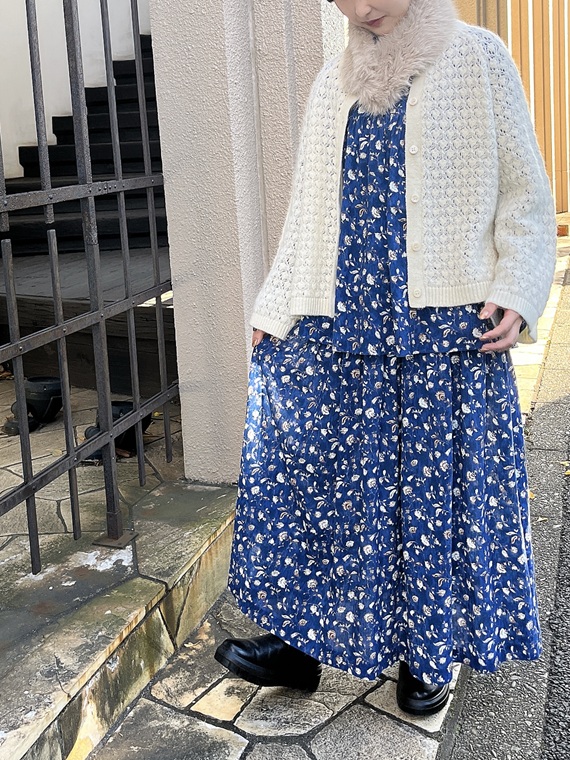 あざやかなコン系のブラウスとスカートをワンピースのようにセットアップし、オフのカーディガンと合わせたコーディネートです。可憐な小花柄のプリントをパイナップルのような地柄のニットで奥行きを持たせて、あたたかな雰囲気を演出しました。
モデル身長：152cm